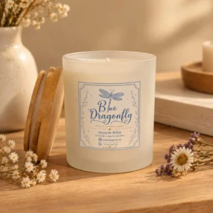 Vela Aura: vela de cera de soya en contenedor de vidrio esmerilado con tapa de bambú y etiqueta Blue Dragonfly, sobre mesa de madera clara con flores secas